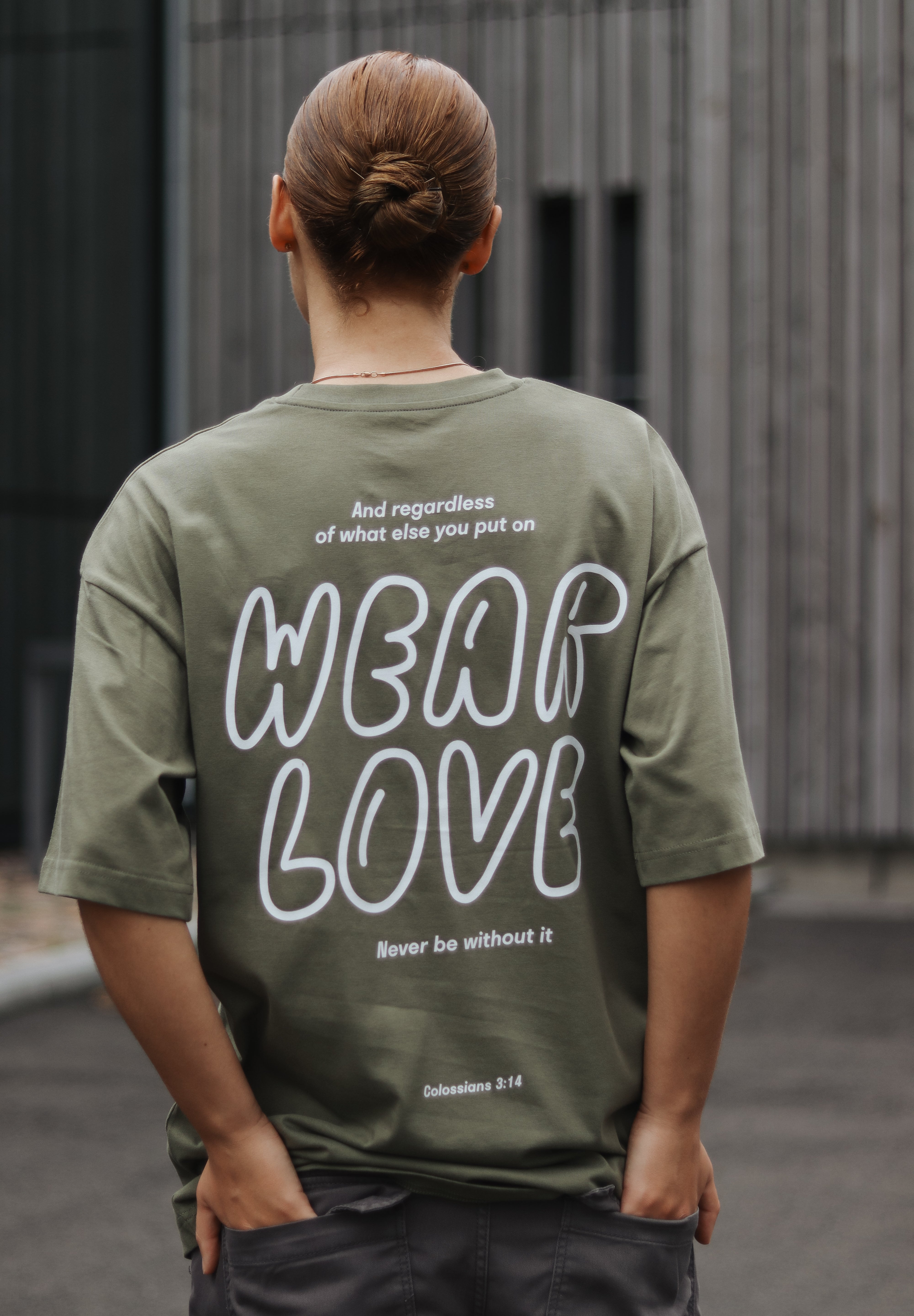 Person wearing a green t-shirt with 'Wear Love' text on the back, standing outdoors.