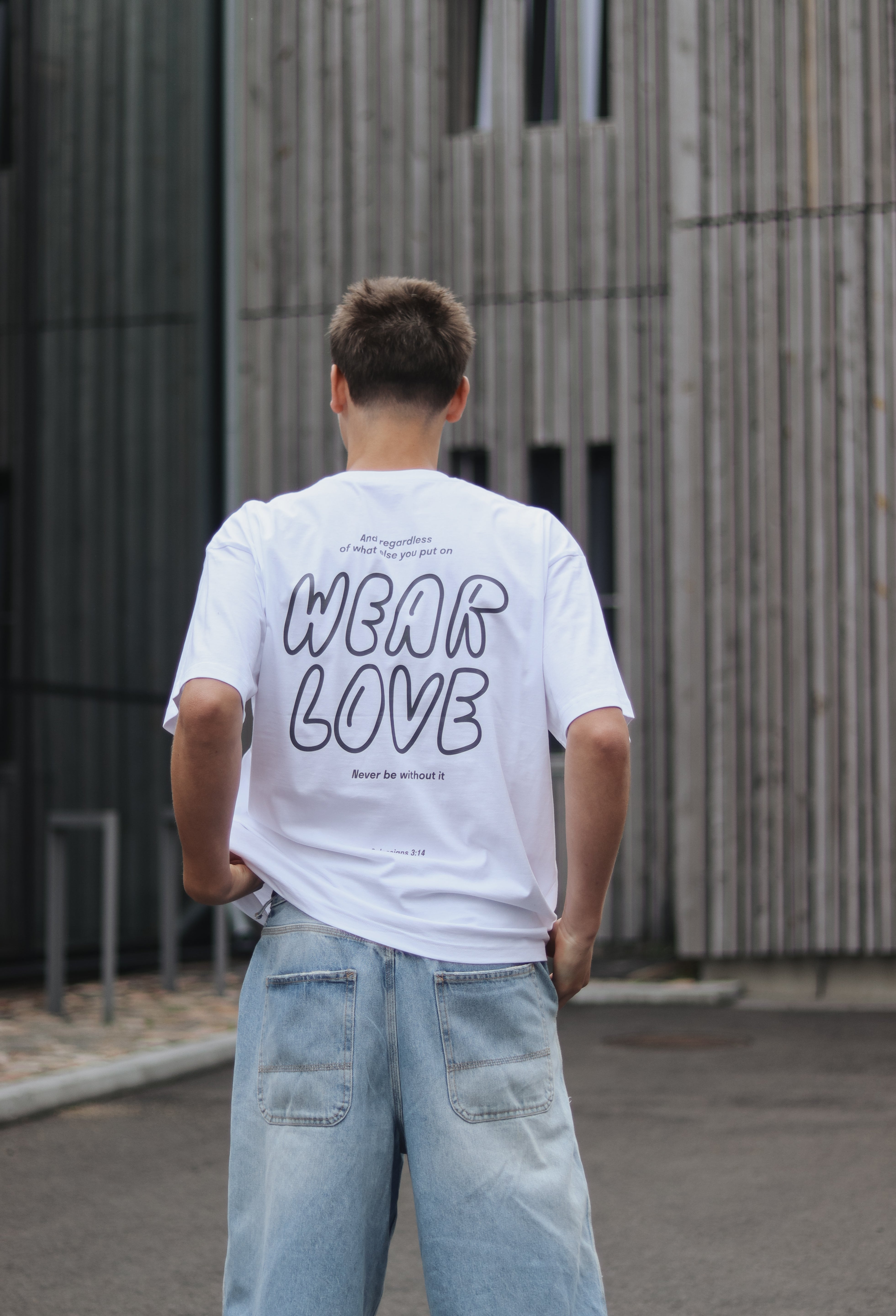 Person wearing a white t-shirt with 'WEAR LOVE' text, standing in front of a modern building.