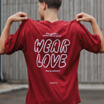 Person wearing a red t-shirt with 'WEAR LOVE' text on the back, standing outdoors.