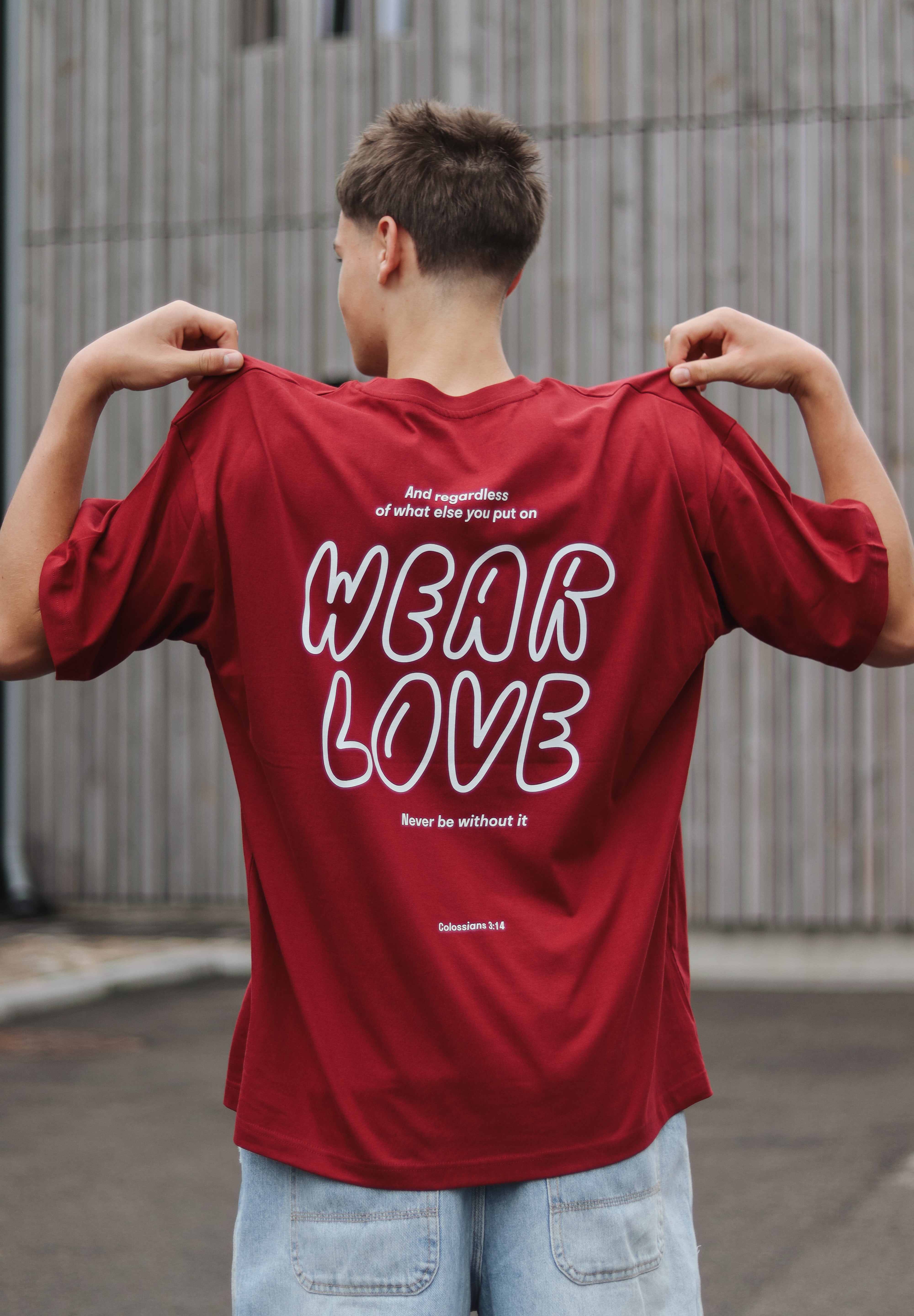Person wearing a red t-shirt with 'WEAR LOVE' text on the back, standing outdoors.