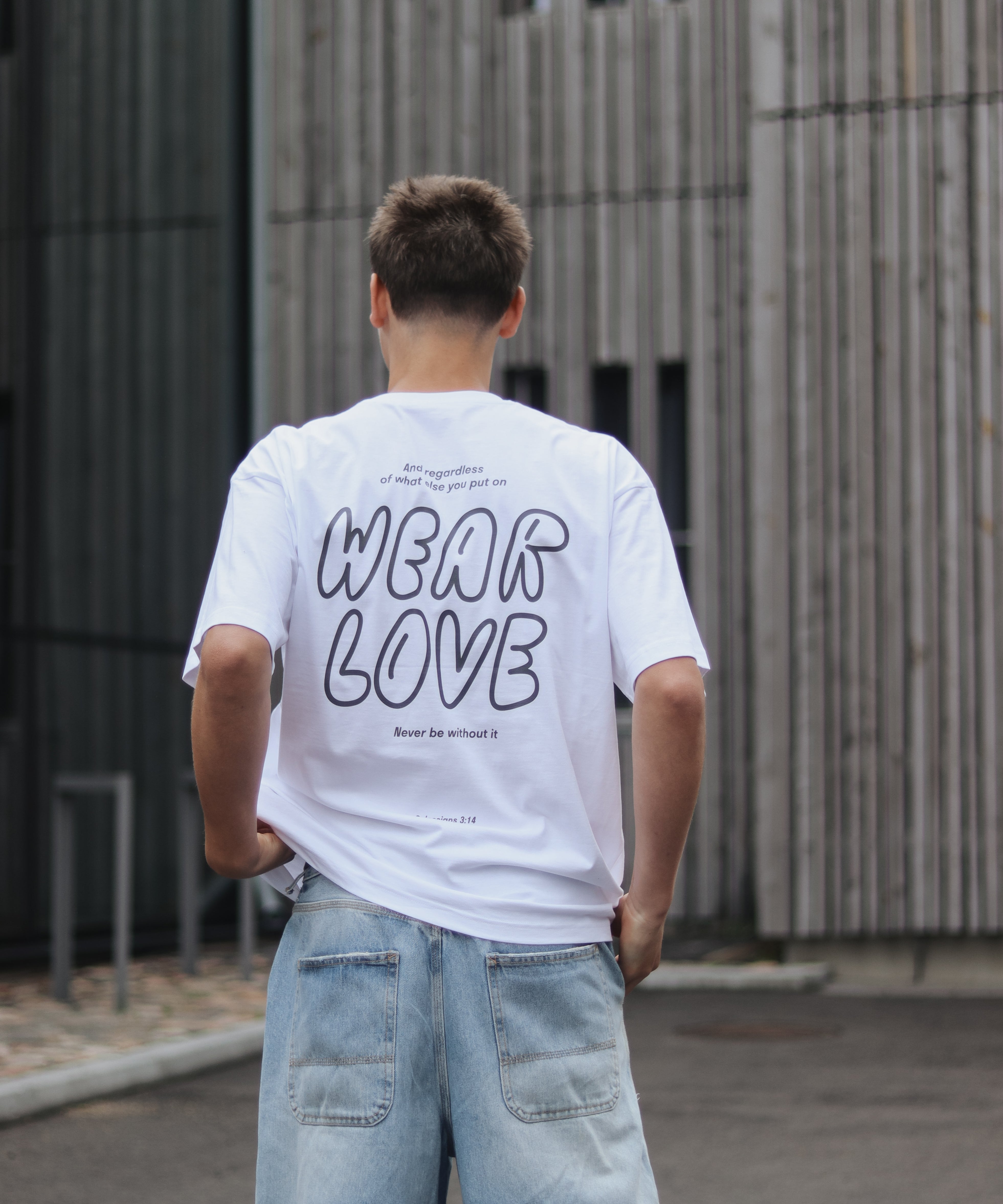 Person wearing a white t-shirt with 'WEAR LOVE' text, standing in front of a modern building.